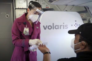 bioseguridad: una azafata de Volaris aplica gel antibacterial en la mano del pasajero de un avión