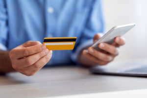 un hombre consulta su smartphone y su tarjeta de crédito