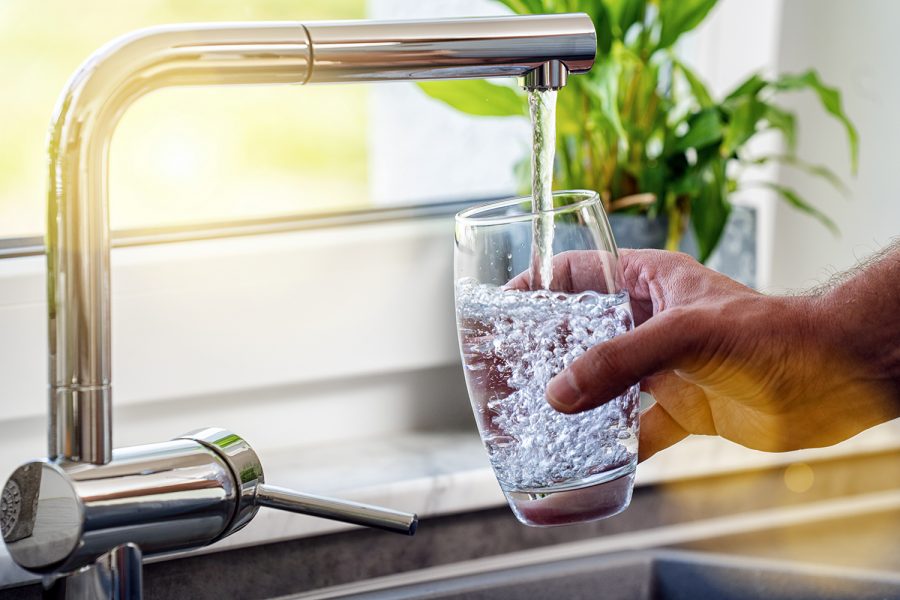 un hombre llena un vaso de agua del grifo de la cocina