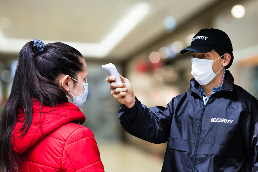 un guardia de seguridad privada toma la temperatura corporal a una cliente de un centro comercial