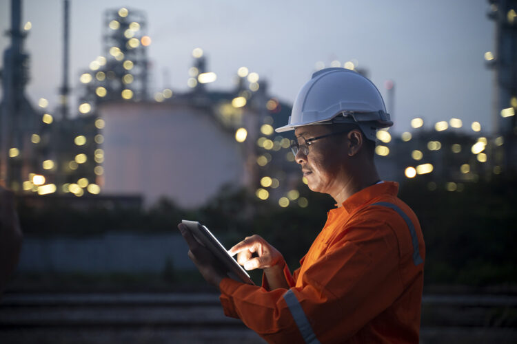 Un operario maneja su tablet junto a una refinería de petróleo