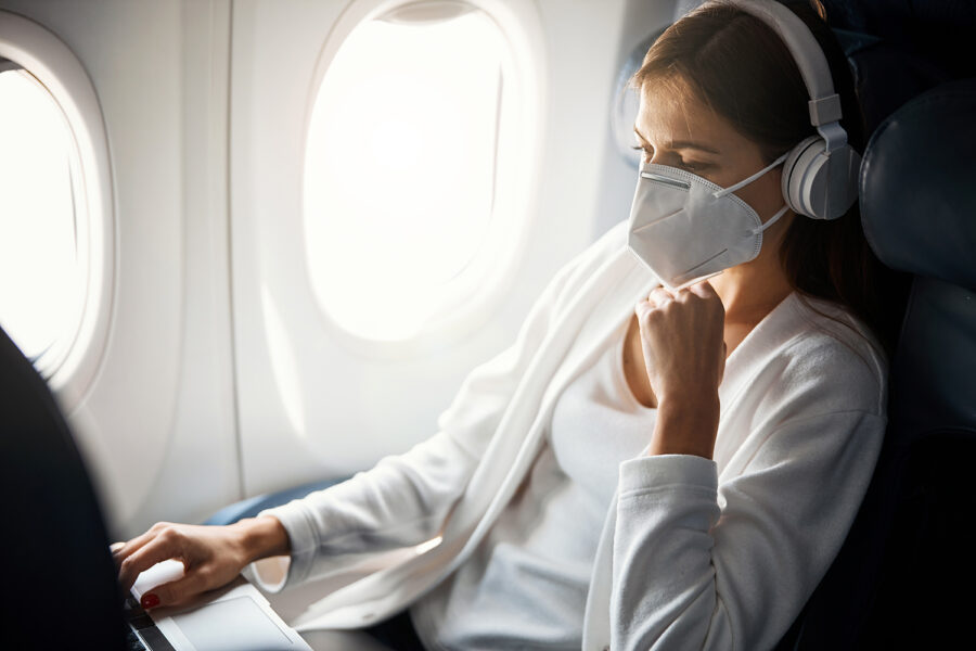 Una mujer con mascarilla escucha música y usa su ordenador en el avión