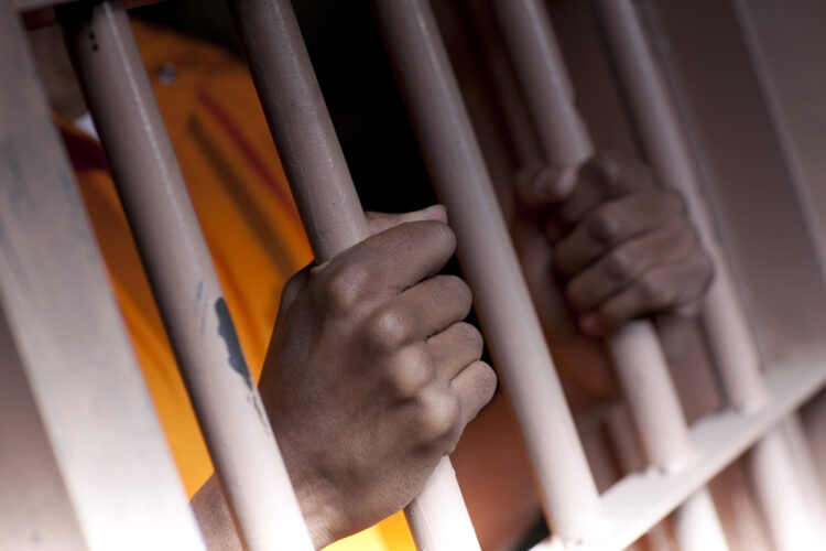 un preso aprieta sus manos en los barrotes de su celda