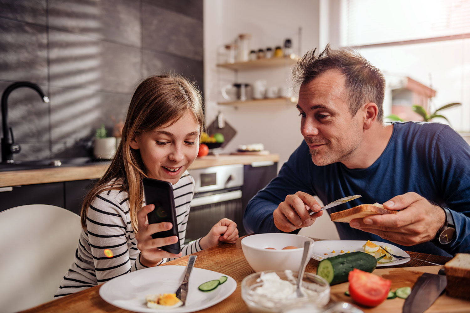 un padre y su hija miran un celular durante el almuerzo