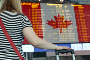 una viajera observa la bandera de Canadá en el panel de vuelos de un aeropuerto