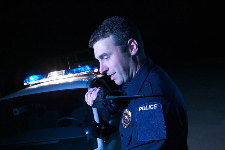 un policía habla a través de su equipo de radio junto a su coche patrulla