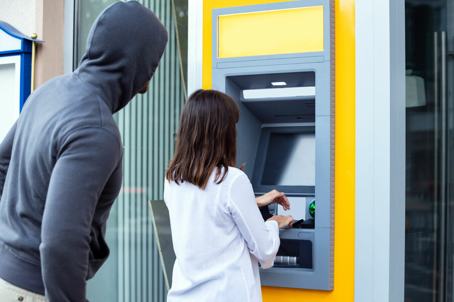 un delincuente observa cómo una mujer saca dinero de un cajero automático