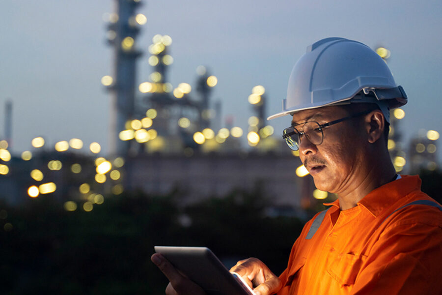 Un operario maneja su tableta electrónica junto a una refinería de petróleo