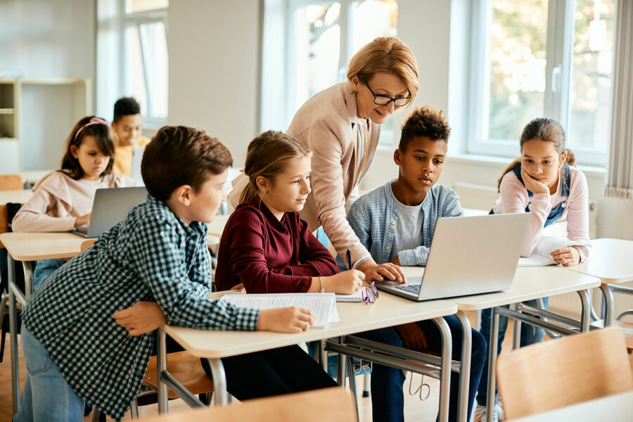una profesora enseña a sus alumnos cómo usar un ordenador portátil