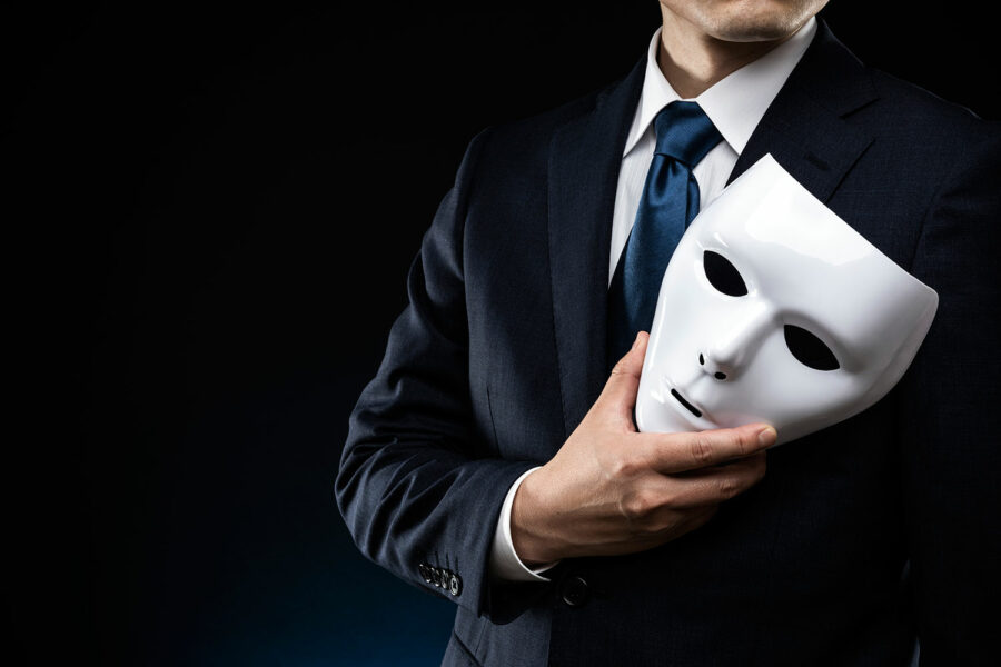 un hombre con traje sostiene una máscara en una mano