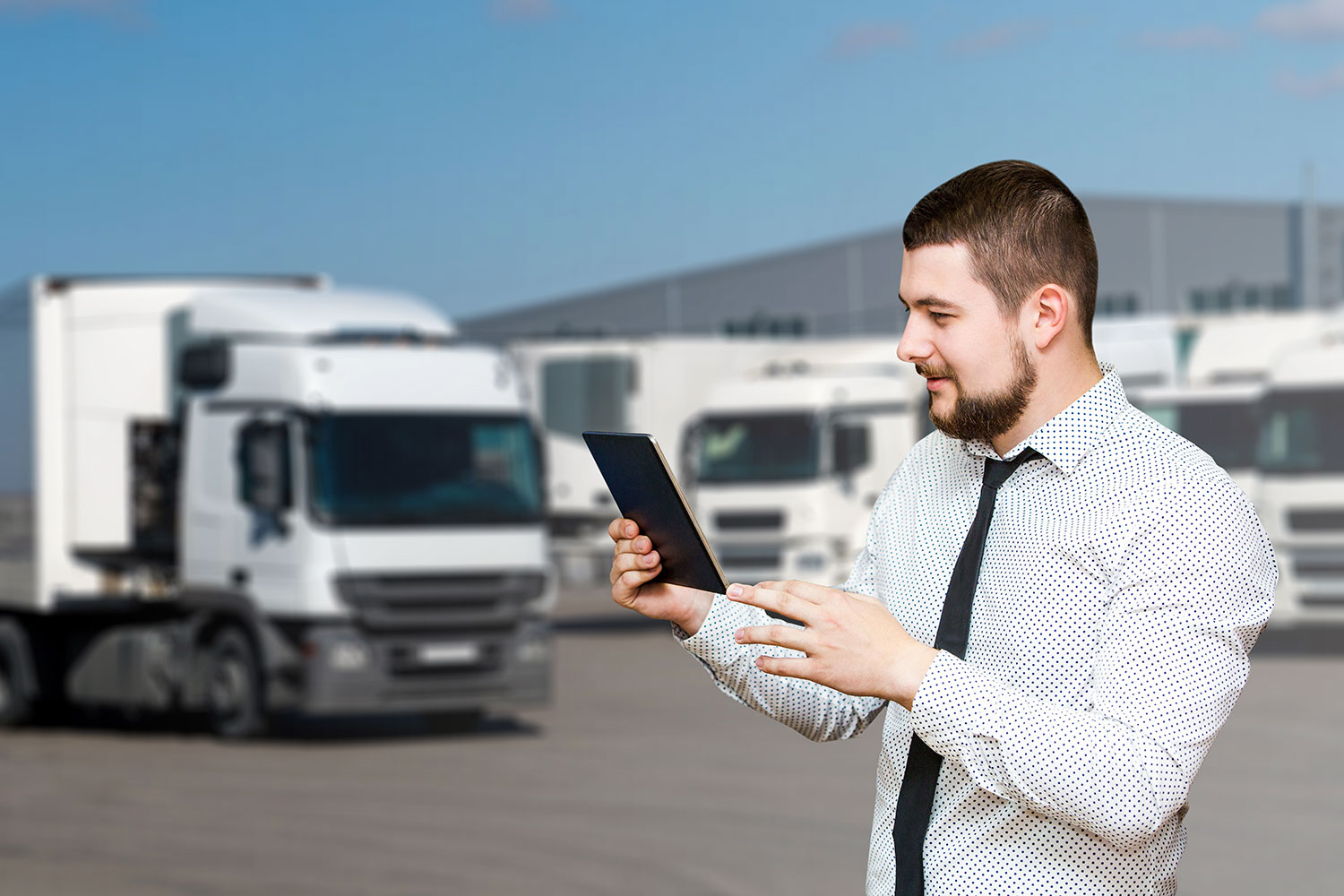un hombre maneja una tablet en un centro de logística con camiones