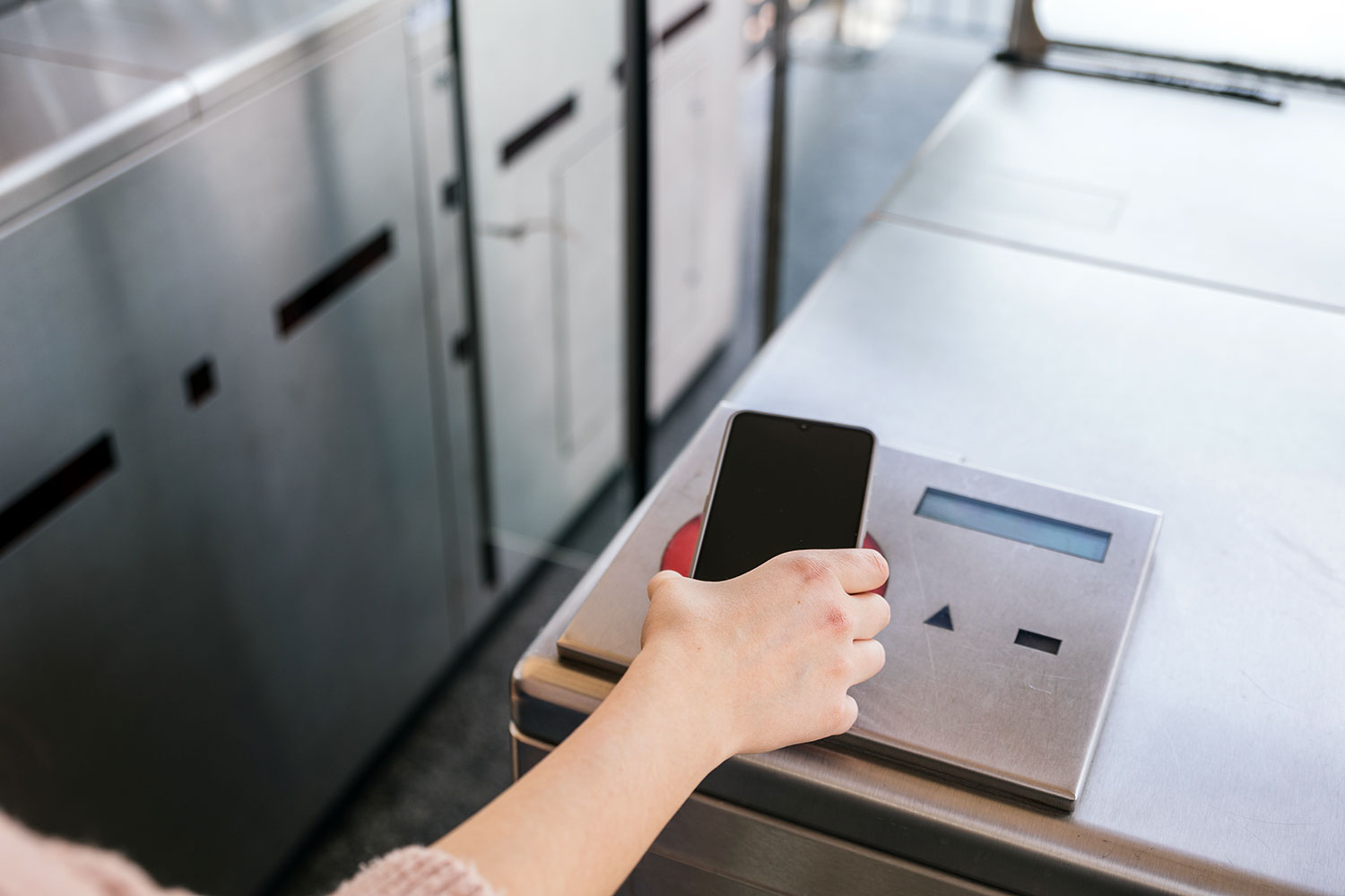 una mujer acerca su teléfono móvil con tecnología NFC al lector de un pasillo de control de accesos