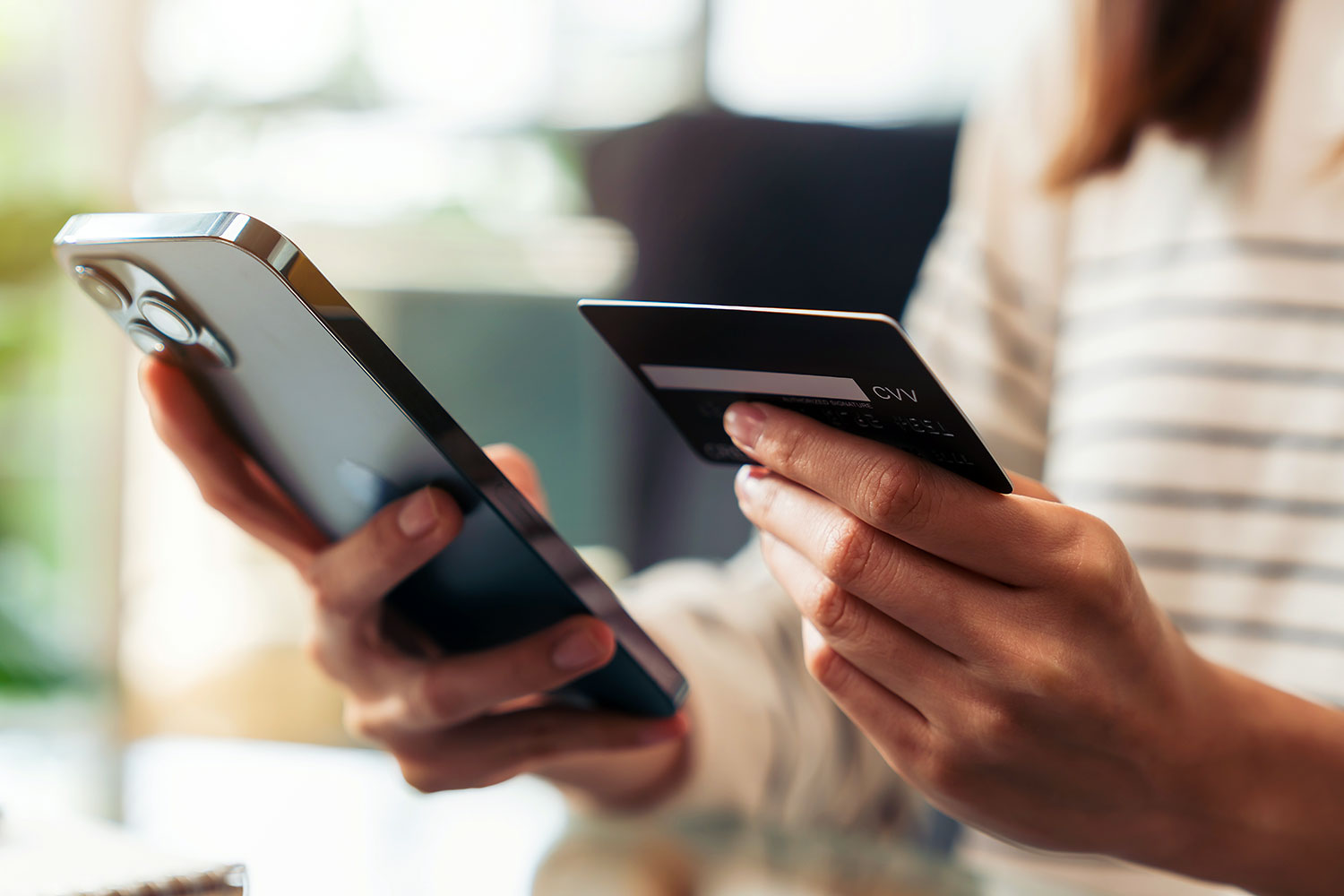 una mujer sostiene un smartphone en una mano y una tarjeta bancaria en la otra