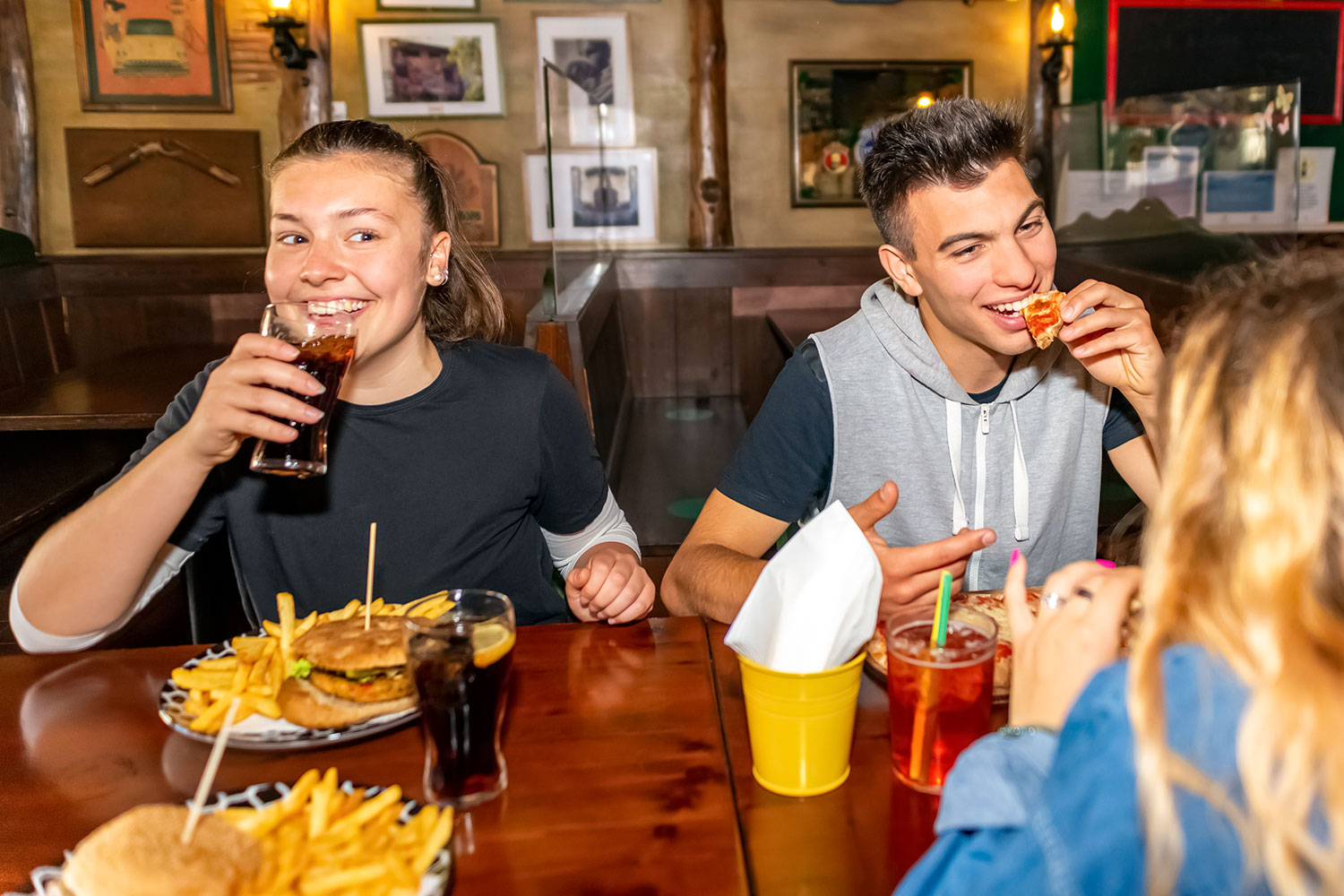 Unos jóvenes consumen hamburguesas, pizzas y refrescos en un bar restaurante