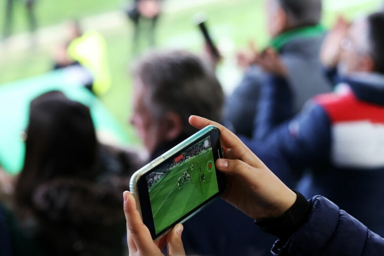 un aficionado graba un partido de fútbol en un estadio con su smartphone