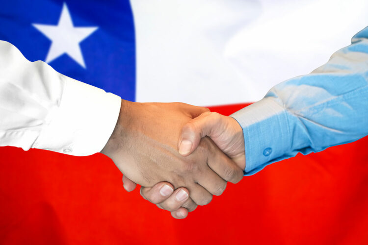 dos personas se dan la mano con la bandera de Chile al fondo