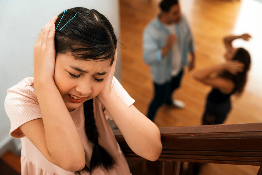 una niña se tapa los oídos mientras sus padres discuten