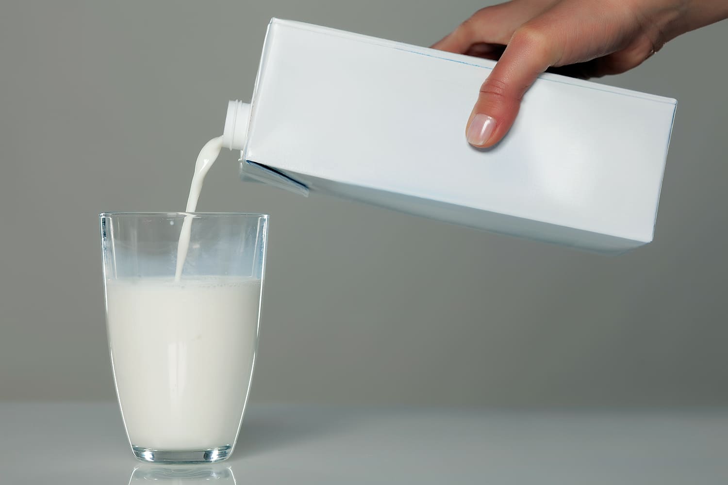 una mujer vierte leche en un vaso de cristal