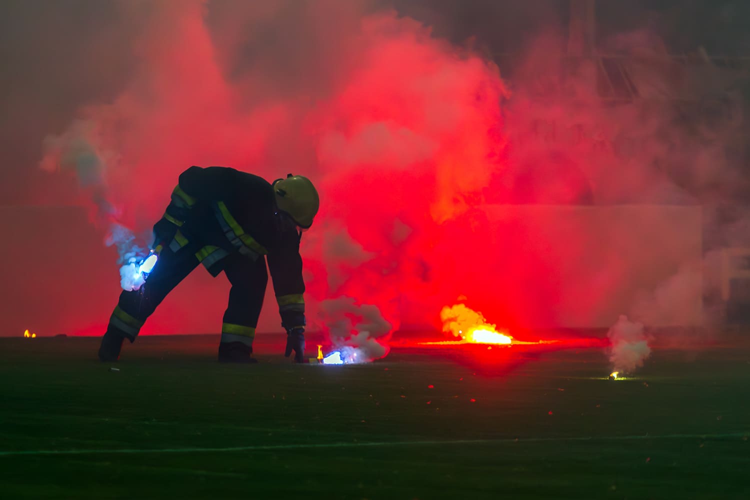 Un bombero recoge bengalas en el terreno de juego de un estadio de fútbol