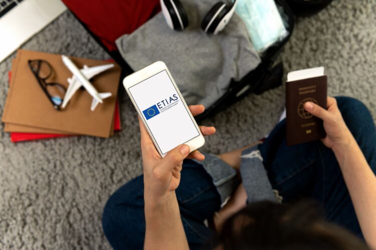 un viajero sostiene un smartphone en una mano con la autorización ETIAS y un pasaporte en la otra mano