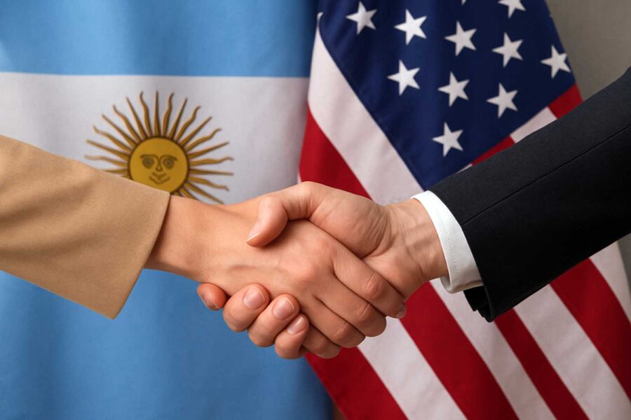 una mujer y un hombre se estrechan la mano con las banderas de Argentina y Estados Unidos detrás