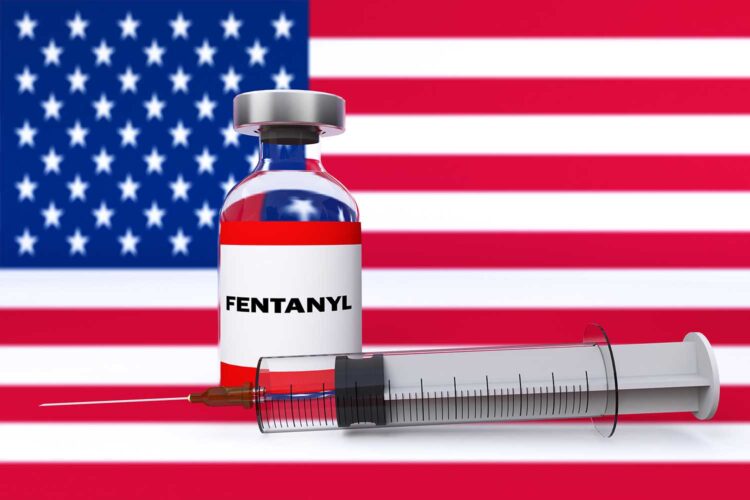 un bote de fentanilo y una jeringuilla con la bandera de Estados Unidos al fondo